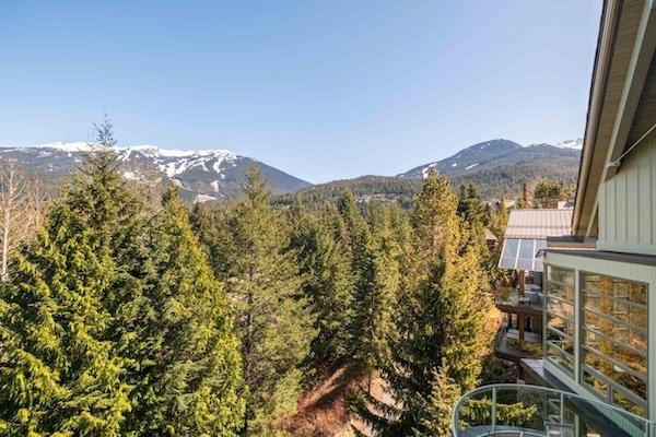 Mountain view Whistler chalet rental with a glass balcony overlooking forest and snow capped peaks.
